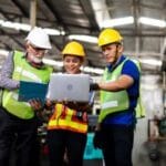 Manufacturing IT Solutions - three people looking at laptop in manufacturing facility